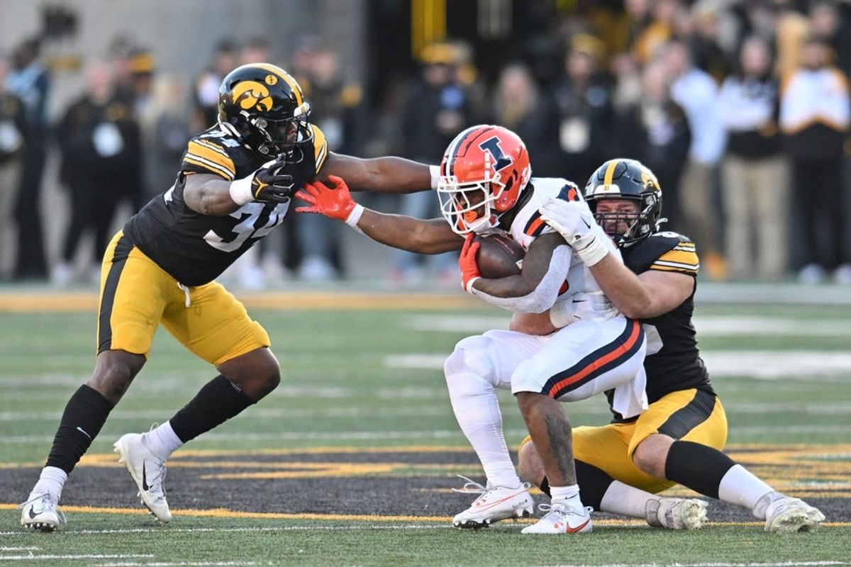 Nov 18, 2023; Iowa City, Iowa, USA; Illinois Fighting Illini running back Reggie Love III (23) is tackled by Iowa Hawkeyes defensive lineman Logan Lee (85) and linebacker Jay Higgins (34) during the second quarter at Kinnick Stadium.