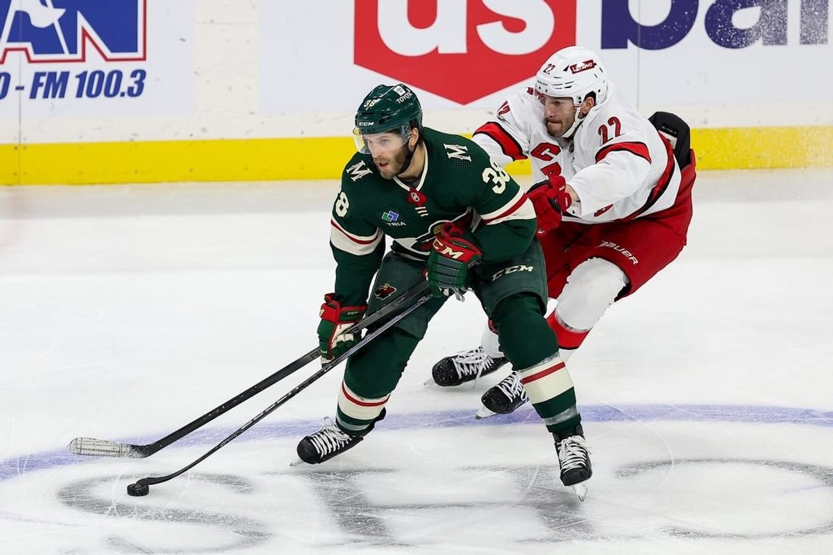 Feb 27, 2024; Saint Paul, Minnesota, USA; Minnesota Wild right wing Ryan Hartman (38) skates with the pucka as Carolina Hurricanes defenseman Brett Pesce (22) defends  during the third period at Xcel Energy Center.