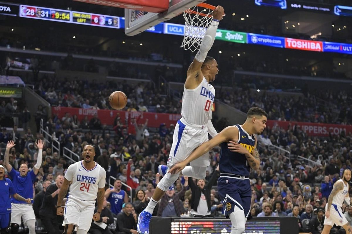 Apr 4, 2024; Los Angeles, California, USA;  Los Angeles Clippers guard Russell Westbrook (0) hangs on the rim after a dunk over Denver Nuggets forward Michael Porter Jr. (1) in the first half at Crypto.com Arena.