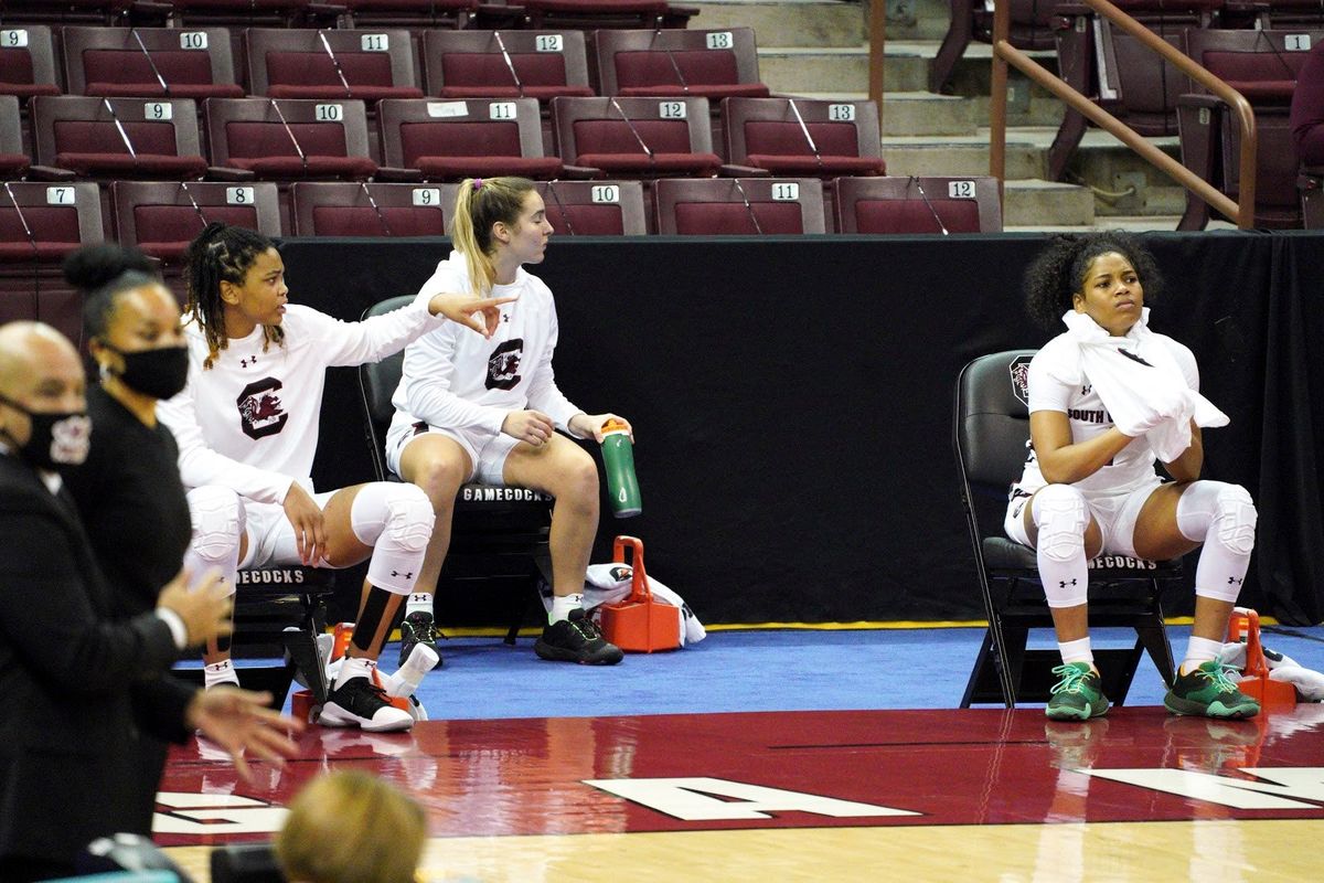 South Carolina guard Zia Cooke (r.) Olivia Thompson, and LeLe Grissett, remain seated during the conclusion of the national anthem, as coaches Dawn Staley and Fred Chmiel, (l.), stand on the sideline before their game.