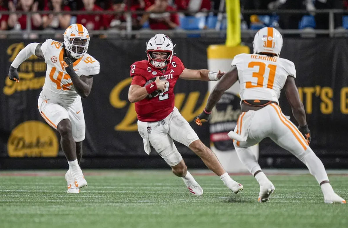 7 de setembro de 2024; Charlotte, Carolina do Norte, EUA; O quarterback do Wolfpack da Carolina do Norte, Grayson McCall (2), corre com a bola enquanto o jogador de linha defensiva do Tennessee Volunteers, Tyre West (42), e o jogador de linha defensiva Caleb Herring (31), defendem durante o segundo tempo no Dukes Mayo Classic no Bank of America Stadium. Crédito obrigatório: Jim Dedmon-Imagn Images