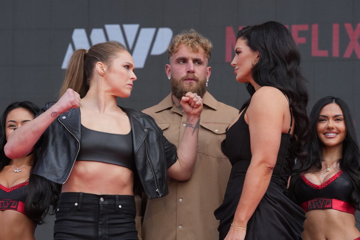 10 de março de 2026; Inglewood, Califórnia, Estados Unidos; Ronda Rousey (à esquerda) e Gina Carano (à direita) se encaram enquanto Jake Paul (ao centro) observa durante uma coletiva de imprensa para a próxima luta de MMA na categoria peso-pena no Intuit Dome. Crédito obrigatório: Kirby Lee-Imagn Images