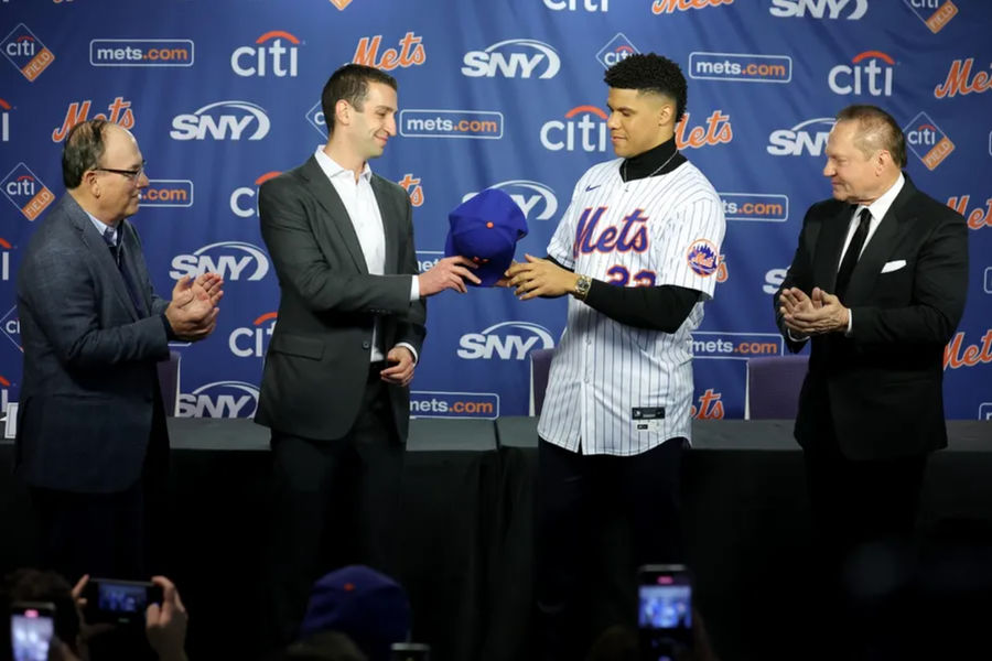 Dec 12, 2024; Flushing, NY, USA; New York Mets general manager David Stearns hands a cap to New York Mets right fielder Juan Soto (22) during Soto's introductory press conference at Citi Field. Also pictured New York Mets owner Steve Cohen (left) and agent Scott Boras (right). Mandatory Credit: Brad Penner-Imagn Images