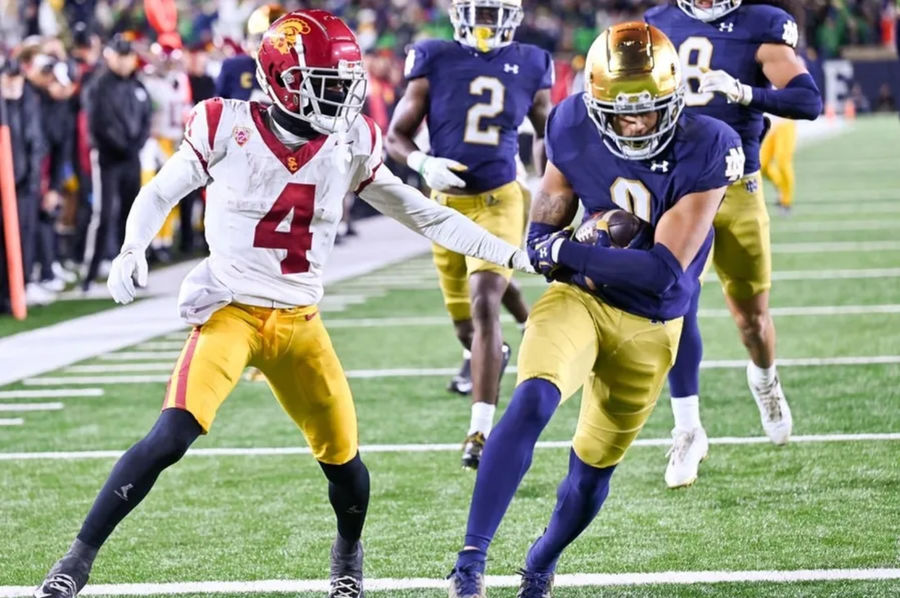 14 de outubro de 2023; South Bend, Indiana, EUA; Notre Dame Fighting Segurança irlandesa Xavier Watts (0) marca um touchdown em frente ao wide receiver do USC Trojans, Mario Williams (4), após uma recuperação de fumble no quarto trimestre no estádio Notre Dame. Notre Dame venceu 48-20. Créditos: Matt Cashore-USA Today Sports