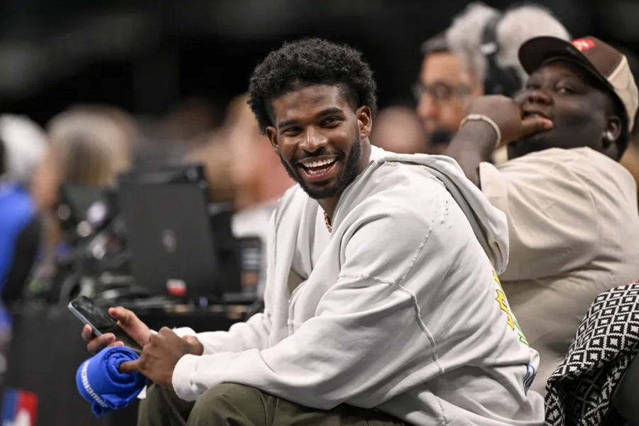 Jan 14, 2025; Dallas, Texas, USA; Colorado Buffaloes quarterback Shedeur Sanders laughs as he watches the game between the Dallas Mavericks and the Denver Nuggets during the second half at the American Airlines Center. Mandatory Credit: Jerome Miron-Imagn Images