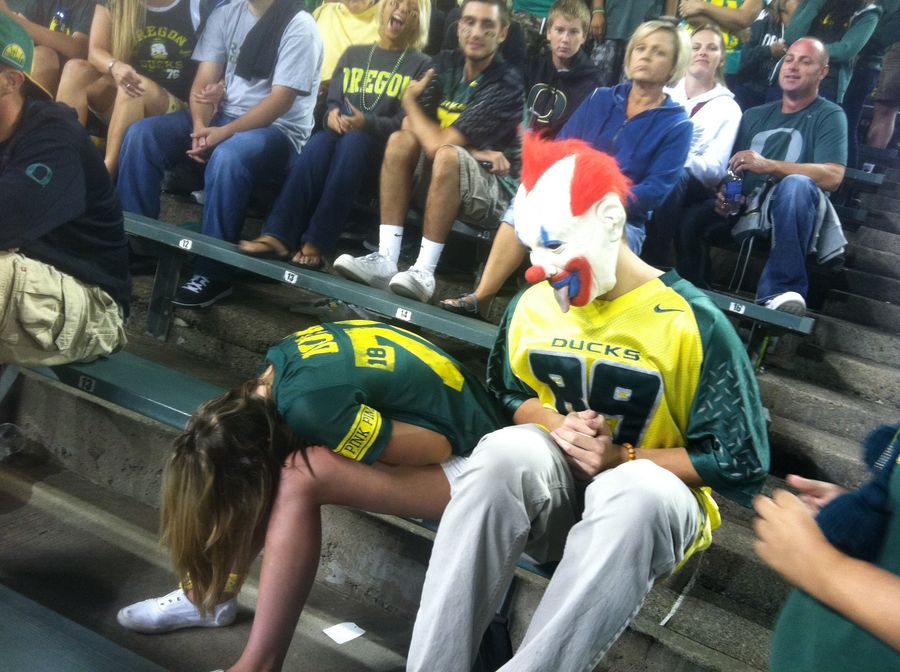 There's A Lot Going On In This Photo Of A Passed-Out Oregon Ducks Fan Being Ogled By A Creepy Clown
